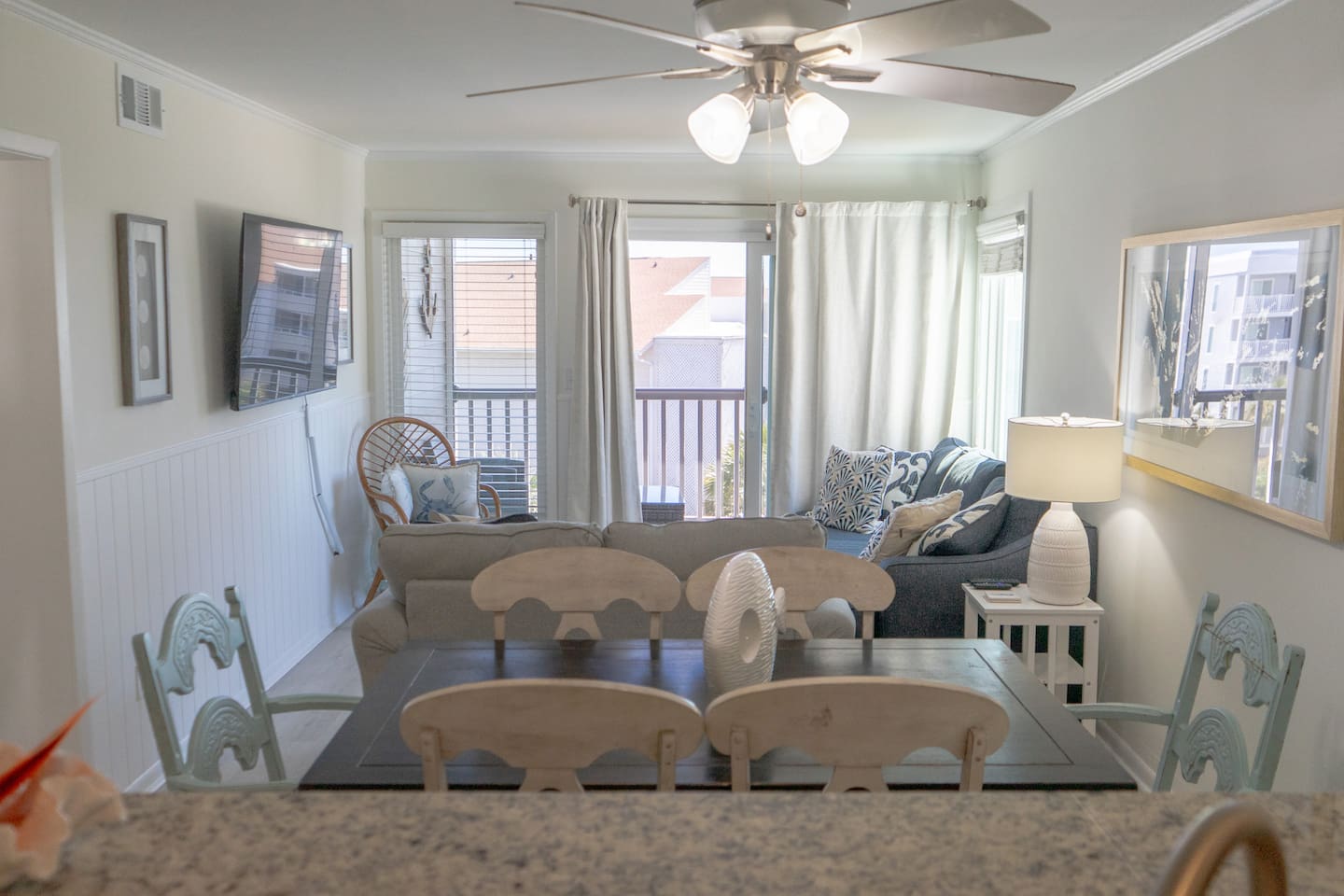 Open living and dining space features cozy seating, beach-inspired décor, and plenty of natural light pouring in from the balcony doors