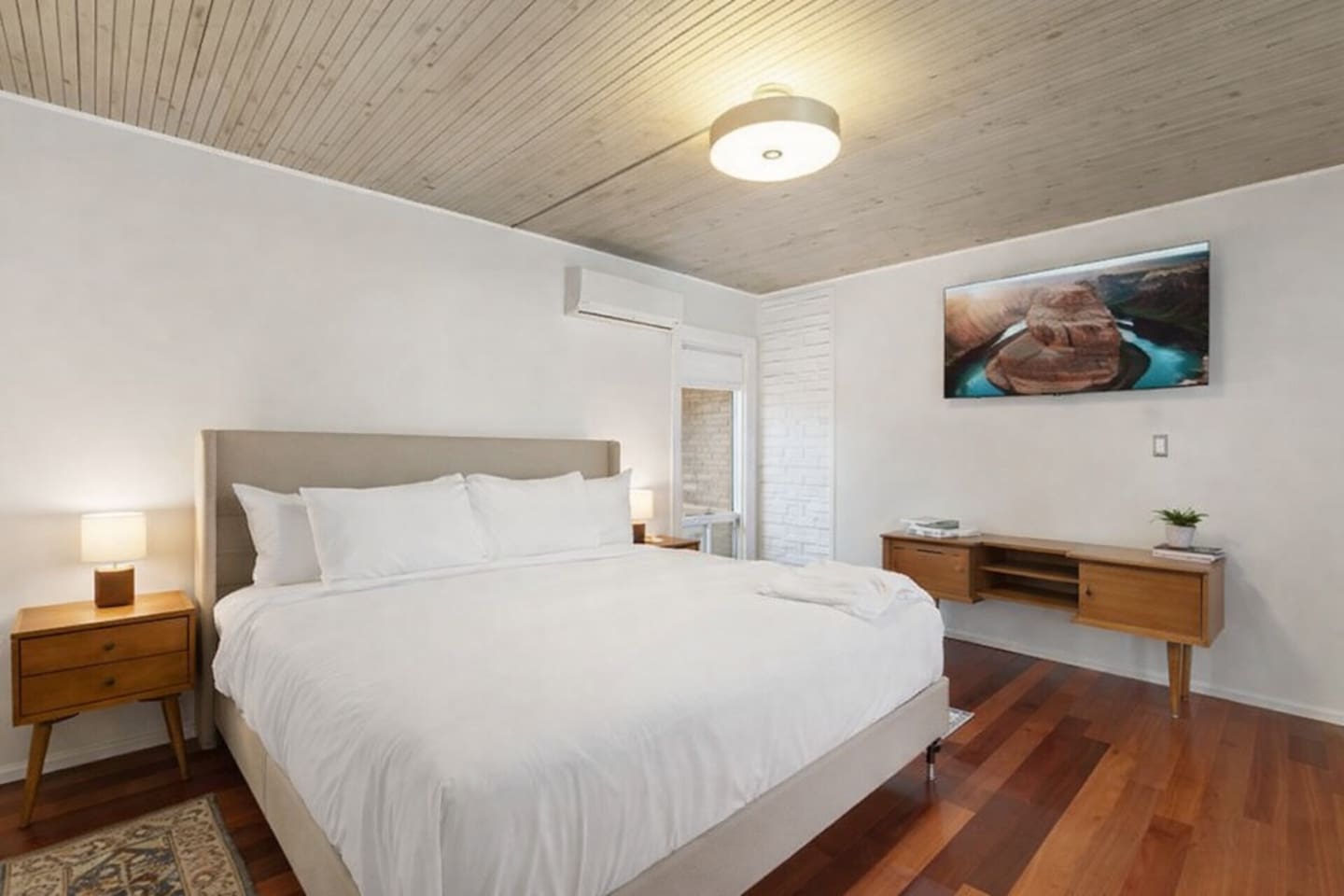 Bright, minimalist bedroom with a king bed, warm wood accents, and a wall-mounted TV for added comfort.