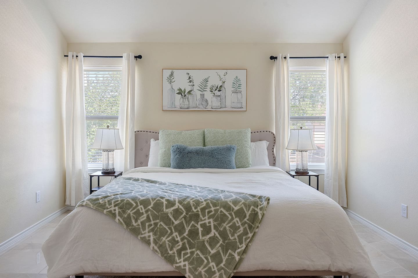 Step into a serene bedroom featuring a cozy bed, stylish bedside lamps, and tasteful botanical wall art.