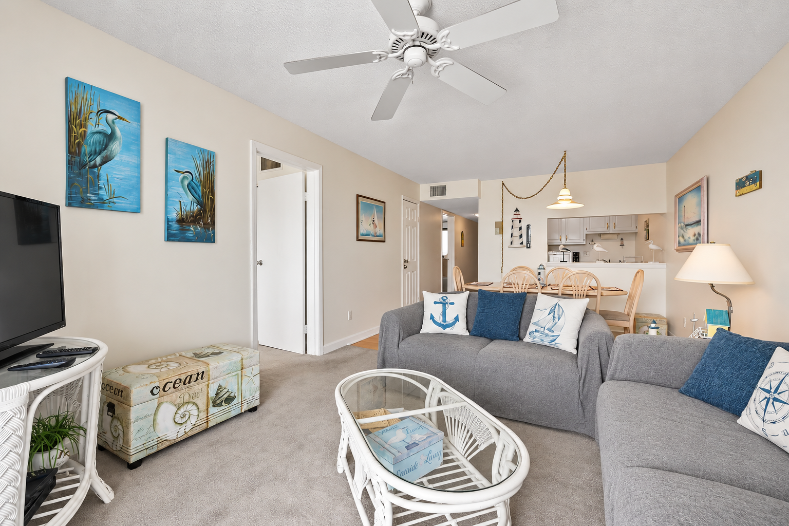 Living room with beach-themed decor, TV seating, and an open view toward the dining area and kitchen.