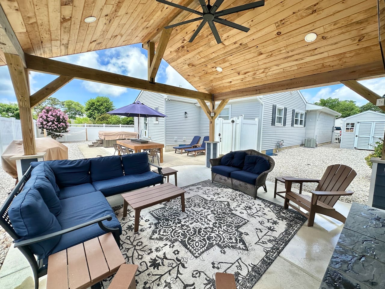Step into your private outdoor sanctuary! This expansive covered patio features a beautiful wood-planked ceiling, plush navy seating, and a stylish rug—the perfect spot to relax and enjoy the fresh coastal breeze.