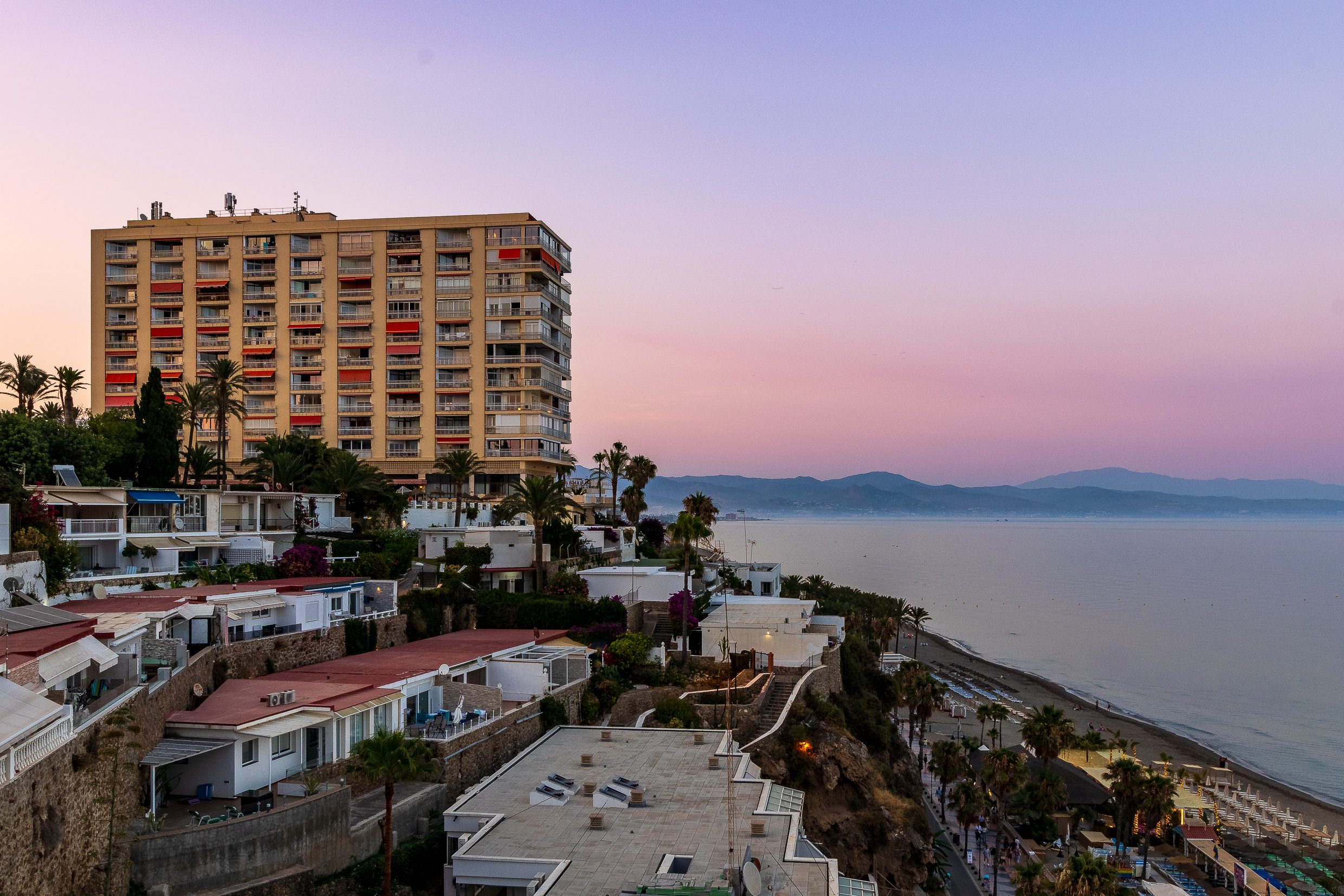 Evening coastline view with the beach, palms and distant mountains.