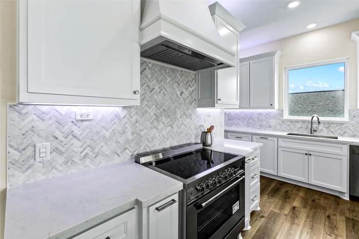 Sleek kitchen with quartz counters, herringbone backsplash, and a modern stainless-steel range.