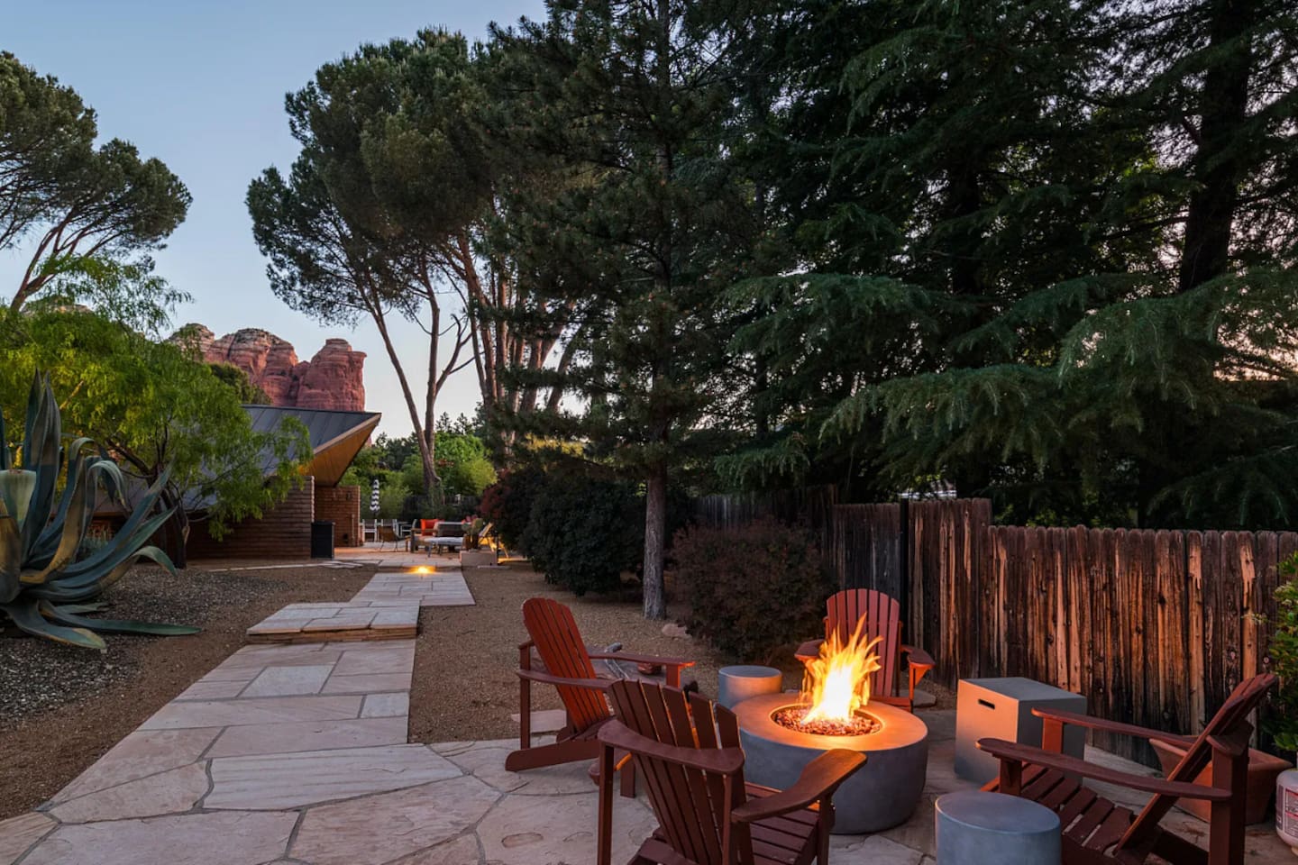 Inviting outdoor retreat featuring a cozy fire pit with Adirondack seating, serene desert landscaping, and stunning red rock views — the perfect spot to unwind under the evening sky.