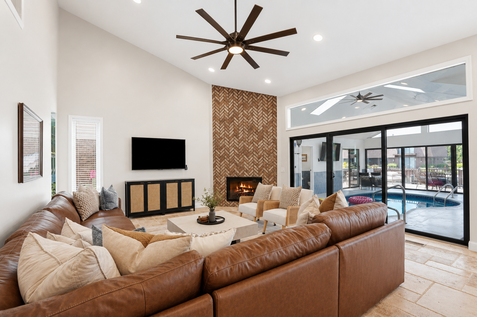 Gather in this spacious open-concept living room featuring a cozy sectional, modern fireplace, soaring ceilings, and seamless indoor-outdoor flow perfect for relaxing and entertaining.