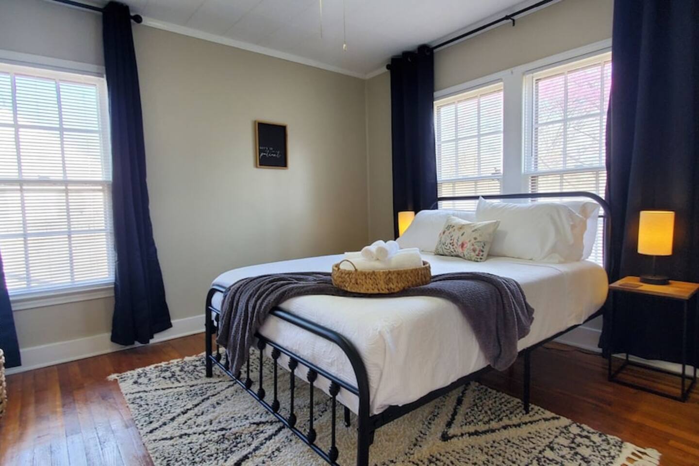 Bright and serene bedroom featuring a cozy queen bed with crisp white linens, soft lighting, and a decorative floral pillow—perfect for a restful stay.