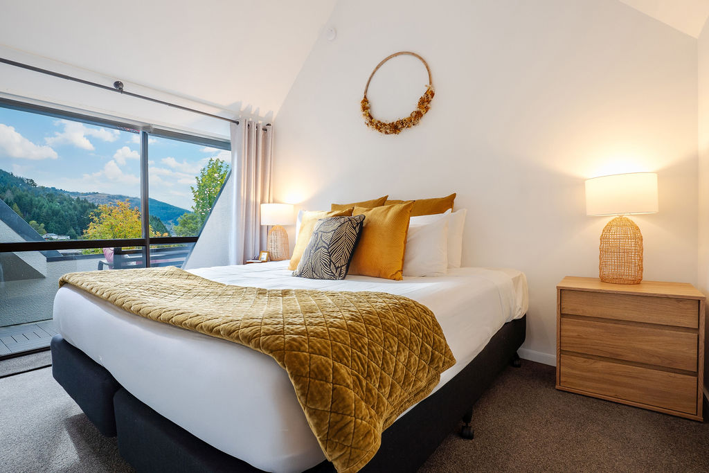 King-single beds, warm bedside lighting and balcony doors give this upstairs bedroom a comfortable setup for the Queenstown stay.