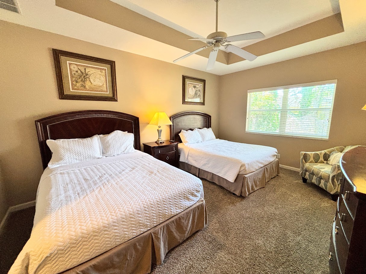 Spacious bedroom featuring two comfortable beds, tray ceiling with ceiling fan, cozy seating area, and plenty of natural light.