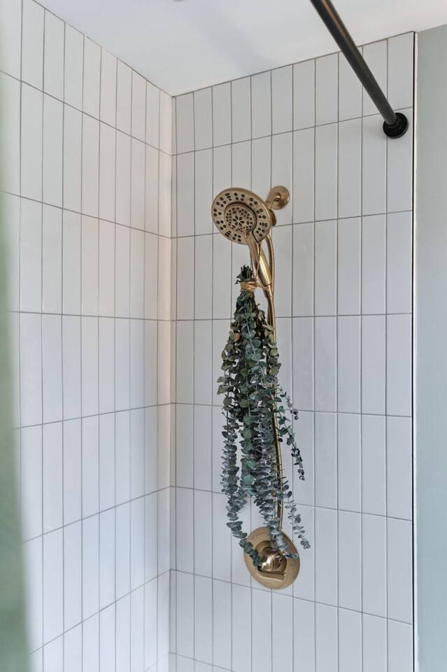 Elegant gold shower fixture paired with clean tilework and a touch of greenery for a fresh, spa-like feel 
