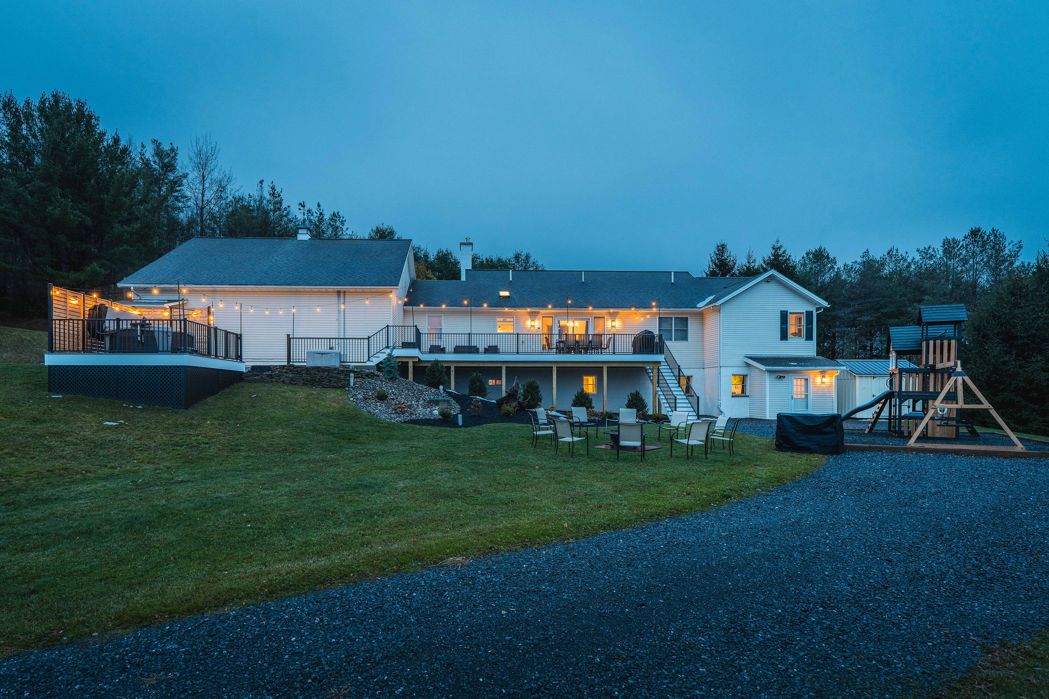Backyard oasis with hot tub, fire pit, deck, and playset all lit beautifully