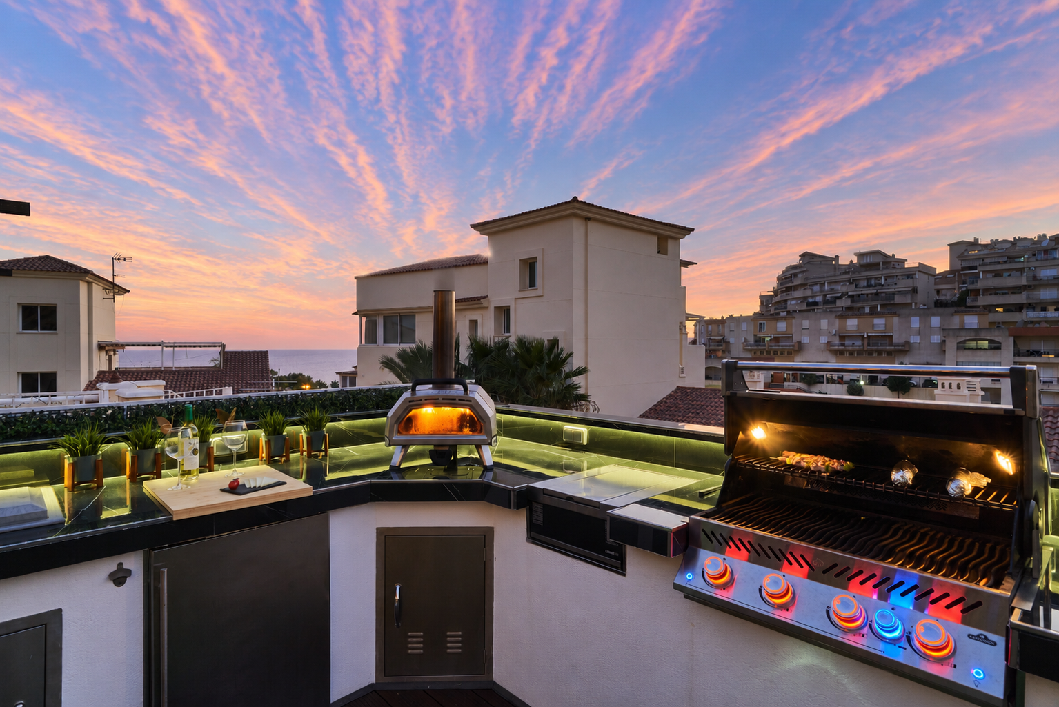 Fire up the built-in barbecue or the wood-fired pizza oven and enjoy cooking with a view. The fully equipped outdoor kitchen features a sink, fridge, and prep space with subtle lighting for evening meals. Dine under the open sky at the outdoor table, surro