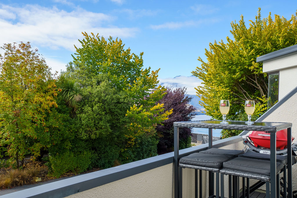 Fernhill Mountain Escape’s balcony catches leafy Fernhill views, with a BBQ, outdoor seating and a Lake Wakatipu glimpse above Queenstown.