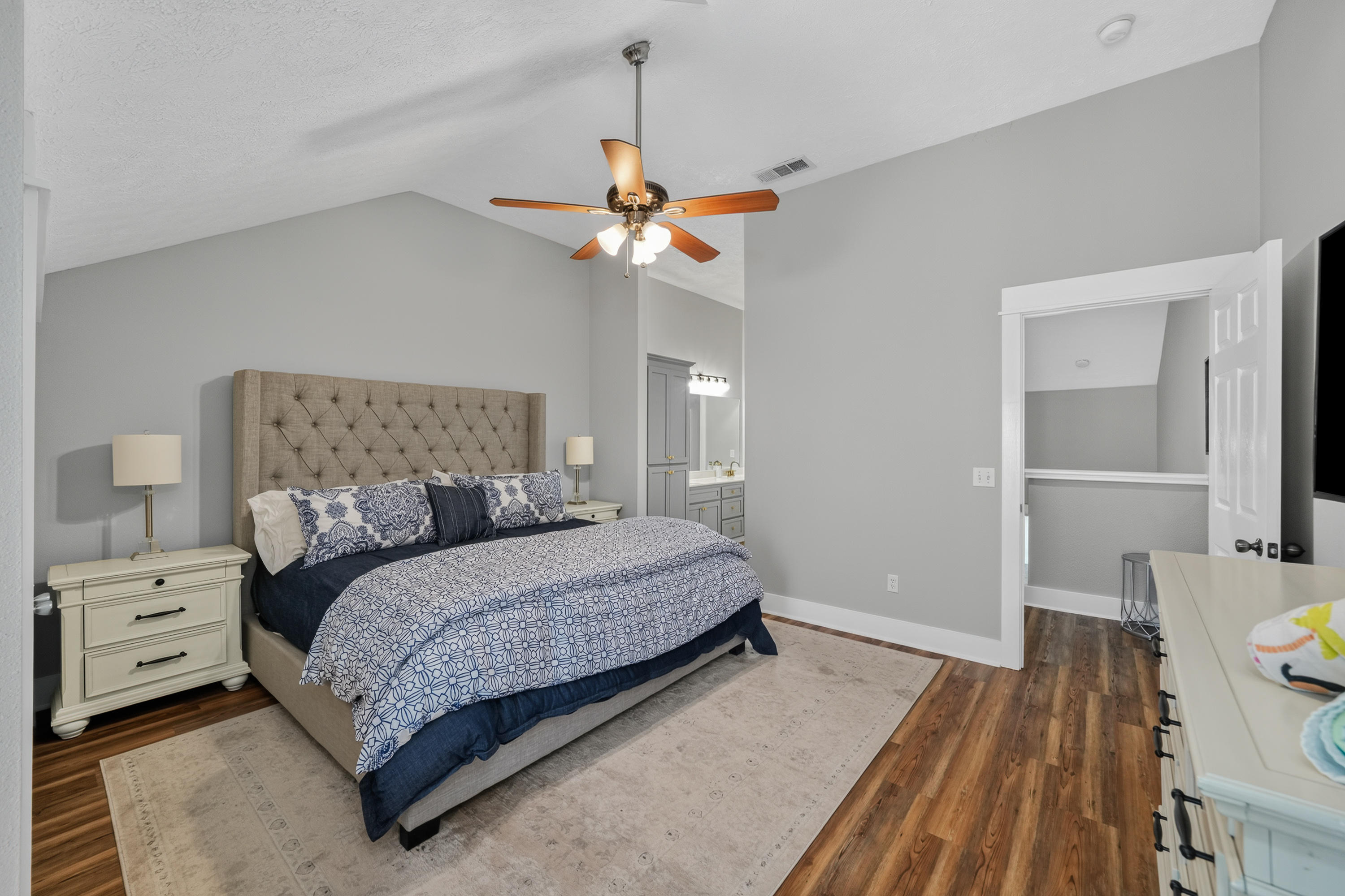 Primary bedroom: with an en-suite bathroom, featuring a king-size bed, premium linens, a ceiling fan, dresser, and night lamp