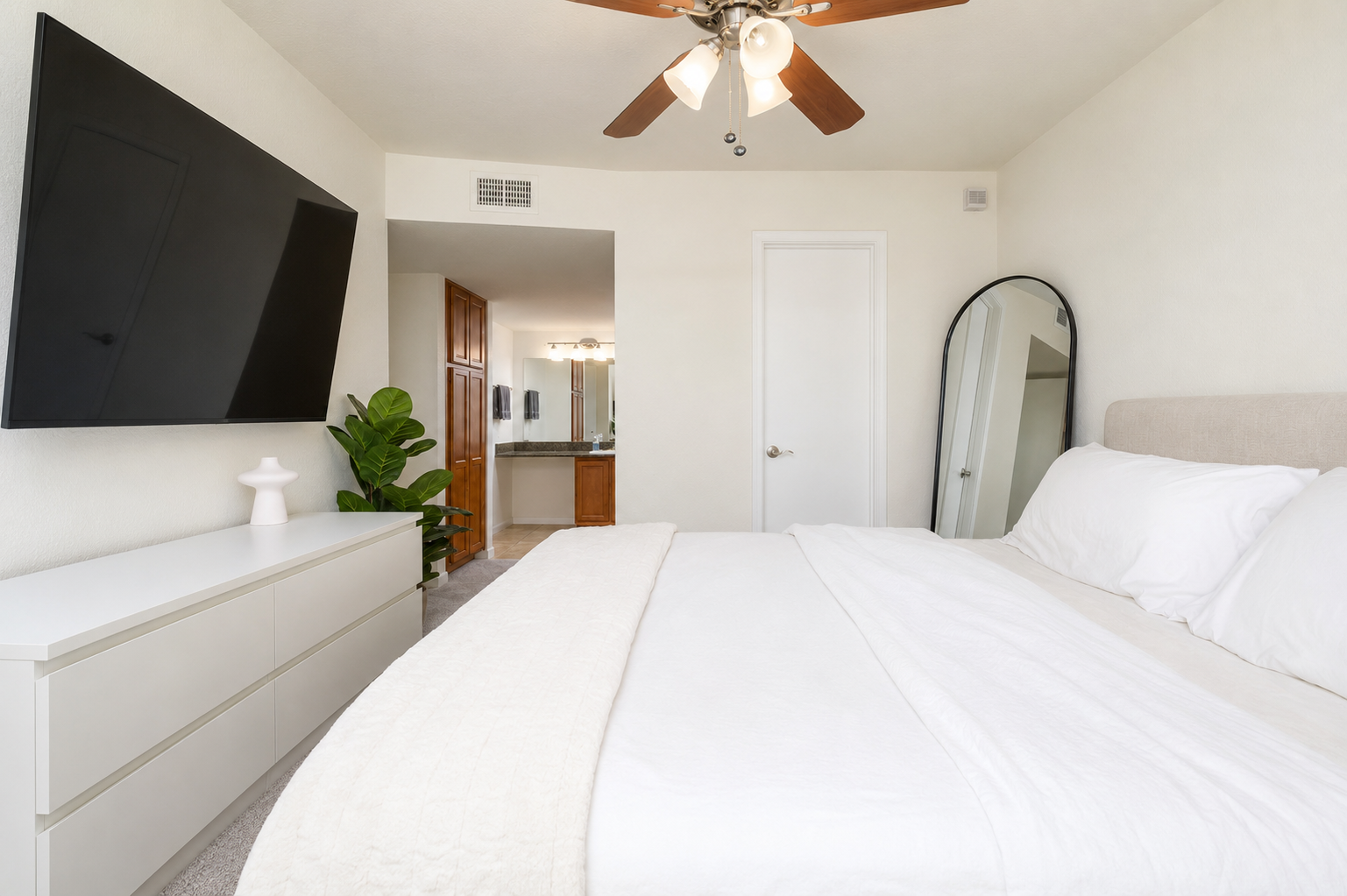 Bedroom with queen bed, wall-mounted TV, ceiling fan, and simple storage for everyday comfort.