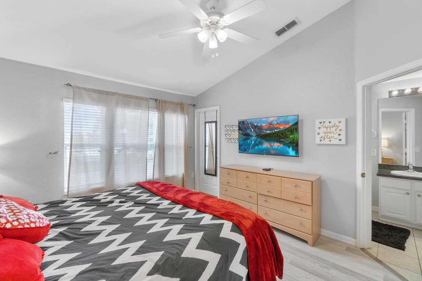 - Sun filled bedroom with king bed, large windows, and soft sheer curtains  
- TV and dresser provide in room entertainment and storage options  
- Connected ensuite and ceiling fan create a comfortable, relaxing escape