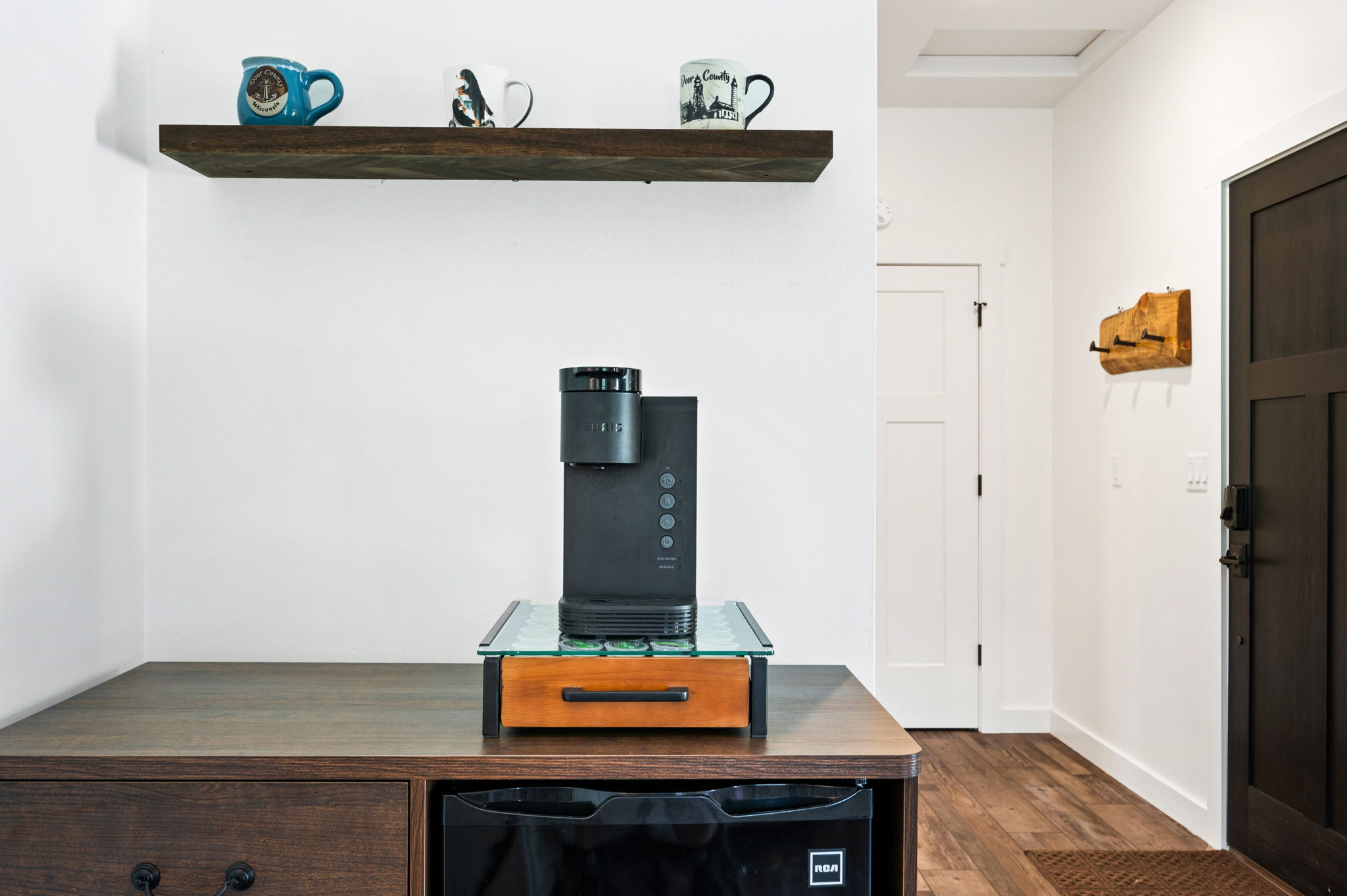 Brew your favorite cup at the in-room coffee bar, stocked with a Keurig, mini-fridge, and Door County mugs on a rustic floating shelf.