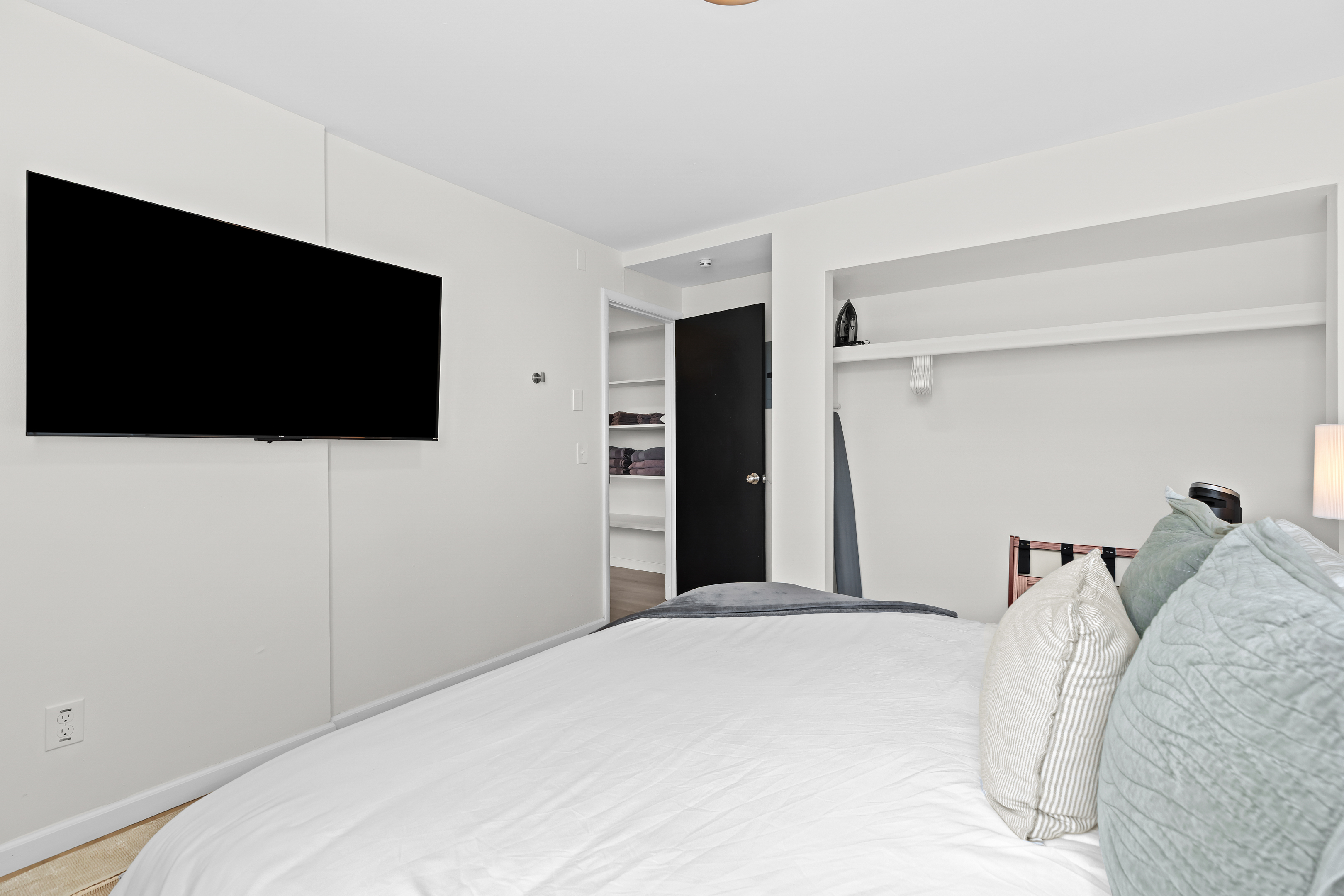 Rest easy in this calming bedroom featuring a mounted smart TV, open shelving, and plenty of extra blankets for your comfort.