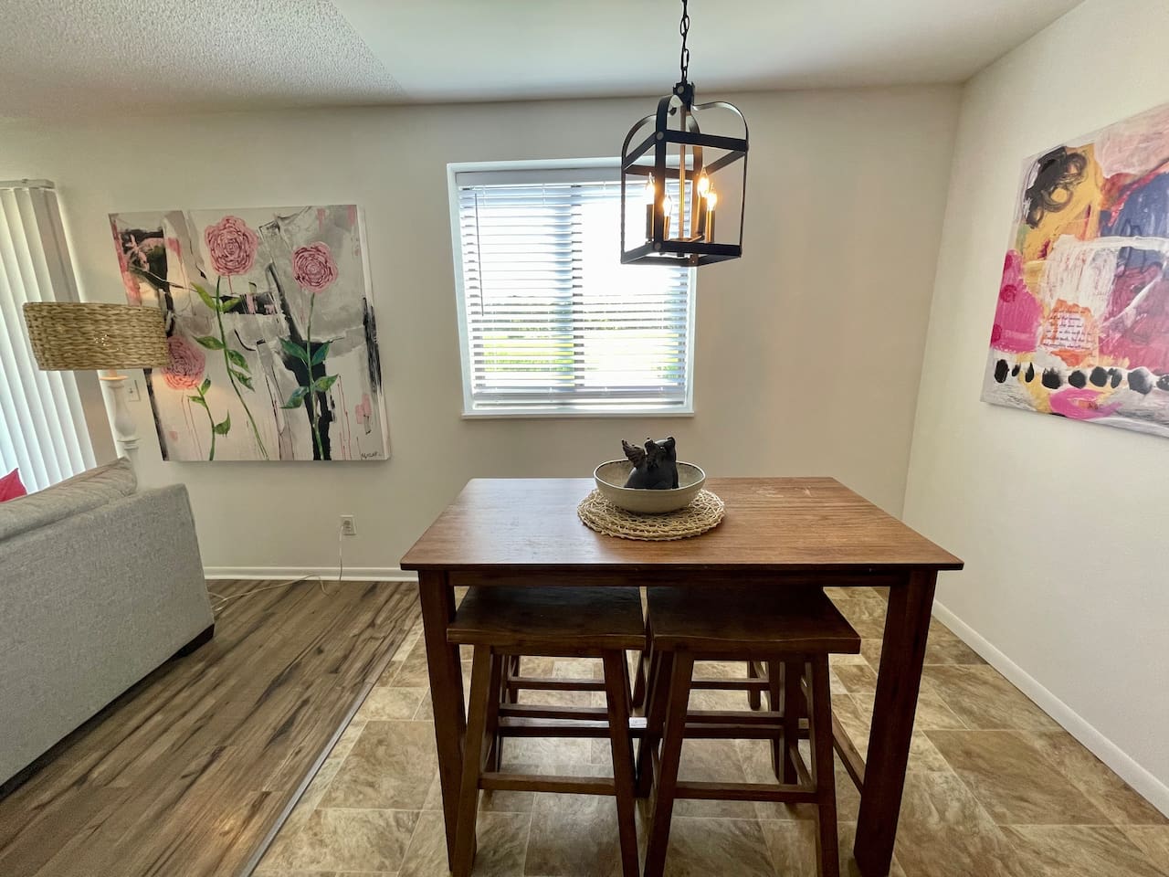 Bright dining area with modern art, natural light, and a cozy wood table for four. A charming lantern-style light fixture adds character, making it a perfect space for meals, board games, or enjoying your morning coffee.