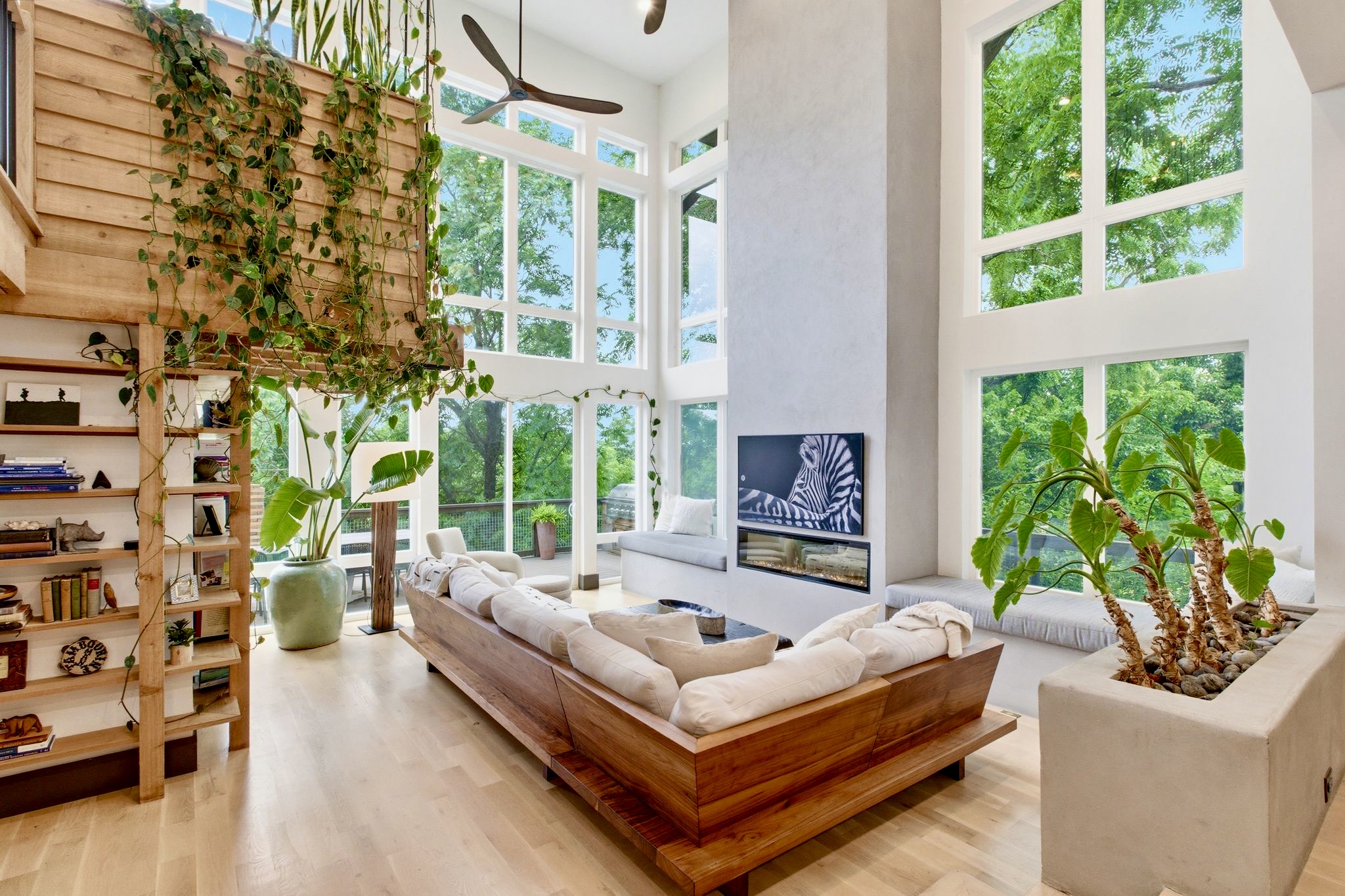 Plant-filled sitting room w/ floor-to-ceiling windows, warm wood accents & a sun-soaked sofa nook.
