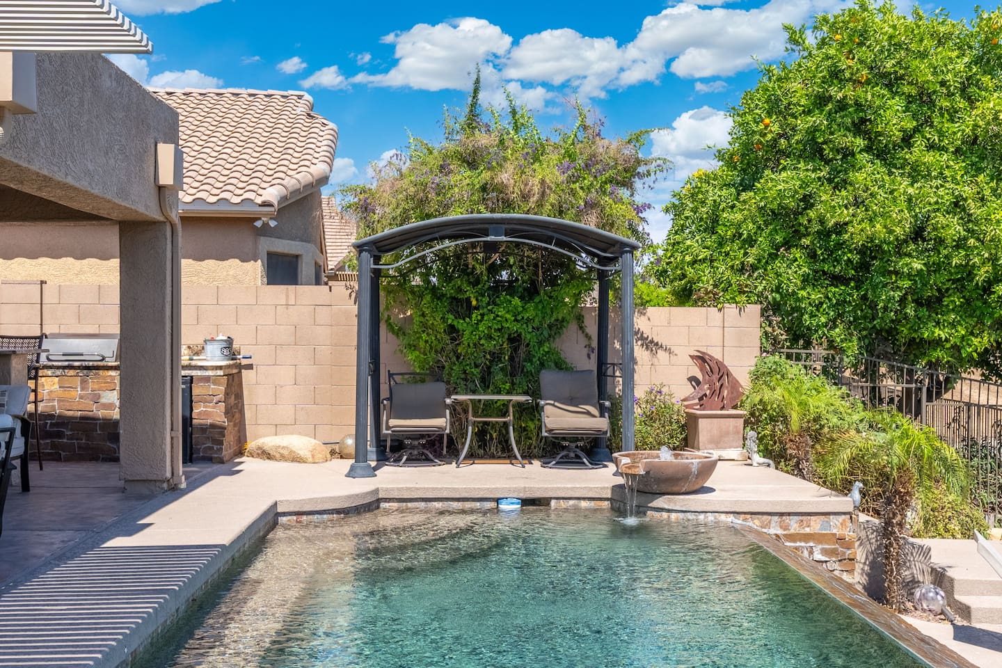 A vine-covered pergola tucked alongside the pool creates a shaded hideaway — the perfect quiet corner to read, nap, or simply enjoy the beauty of the backyard.