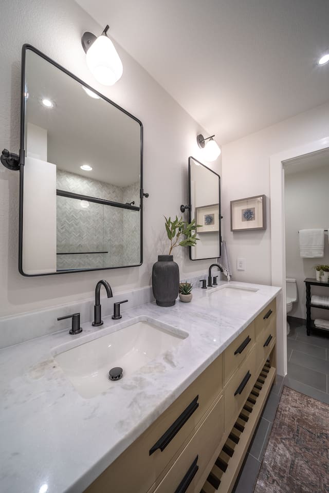 Wide view of the shared hallway bathroom showcasing the double-sink vanity, ample counter space, and a private water closet. Shampoo, conditioner, body wash, and plush towels are provided for guest use.