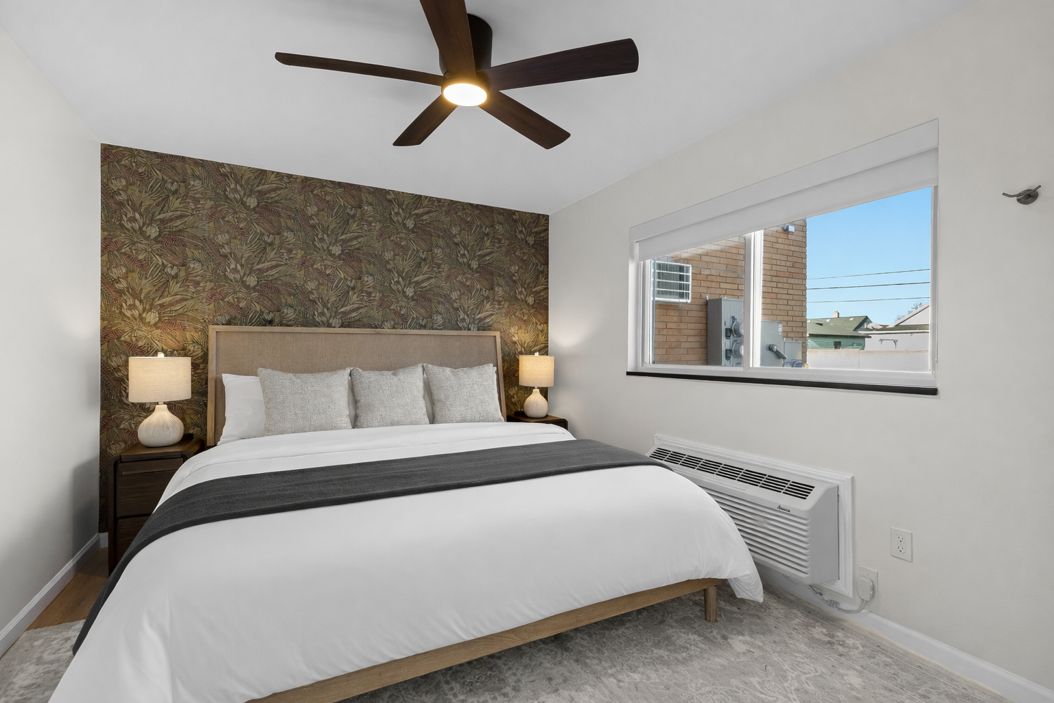 Relax in this serene bedroom featuring a plush bed, stylish accent wall, soft lighting, and a ceiling fan—perfect for restful nights and slow mornings.