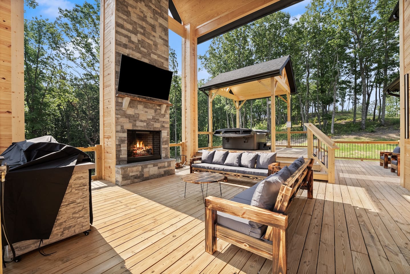 This spacious covered patio is the ultimate entertainment hub, featuring a stone fireplace, mounted TV, comfortable seating, and a BBQ grill for unforgettable evenings.