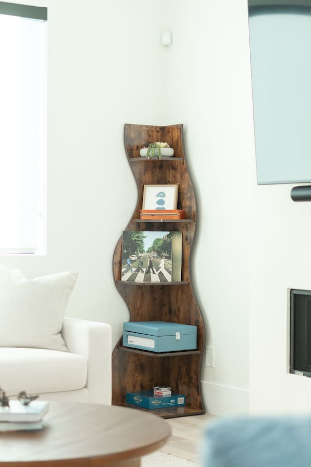 Curved wooden shelf with books, decor, and records adds character and charm to the living room, blending function with style.