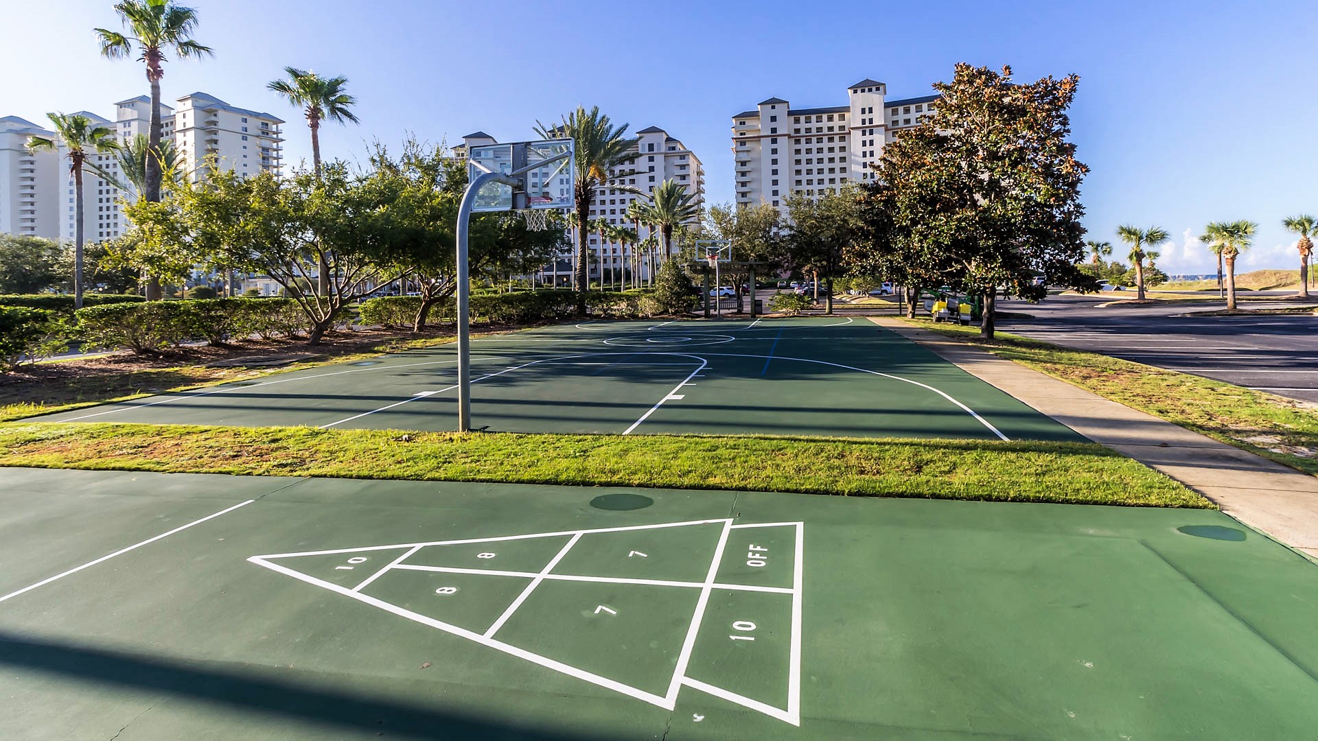 Enjoying the vibrant recreational amenities with a well-maintained basketball court and shuffleboard area, perfect for active leisure under the clear sky.