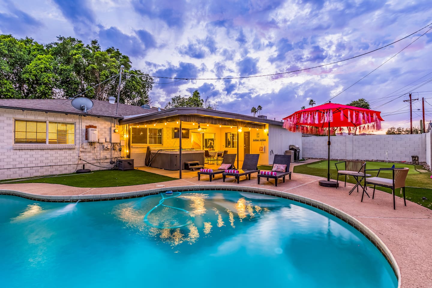 Enjoy evening swims under twinkling string lights in this cozy, well-lit backyard oasis featuring a pool, loungers, and inviting ambiance.

