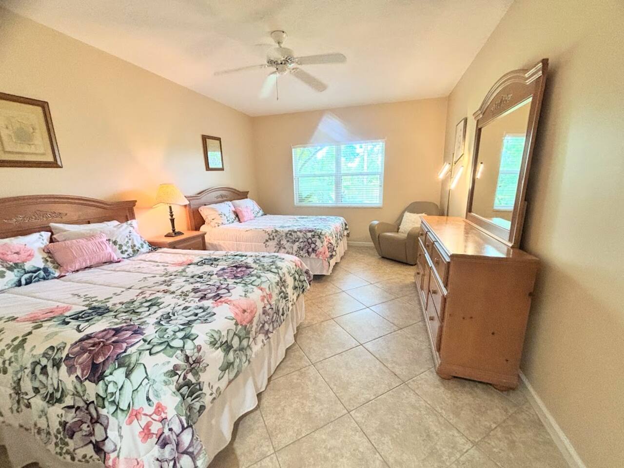 Spacious bedroom with two beds, ceiling fan, dresser storage, and natural light.