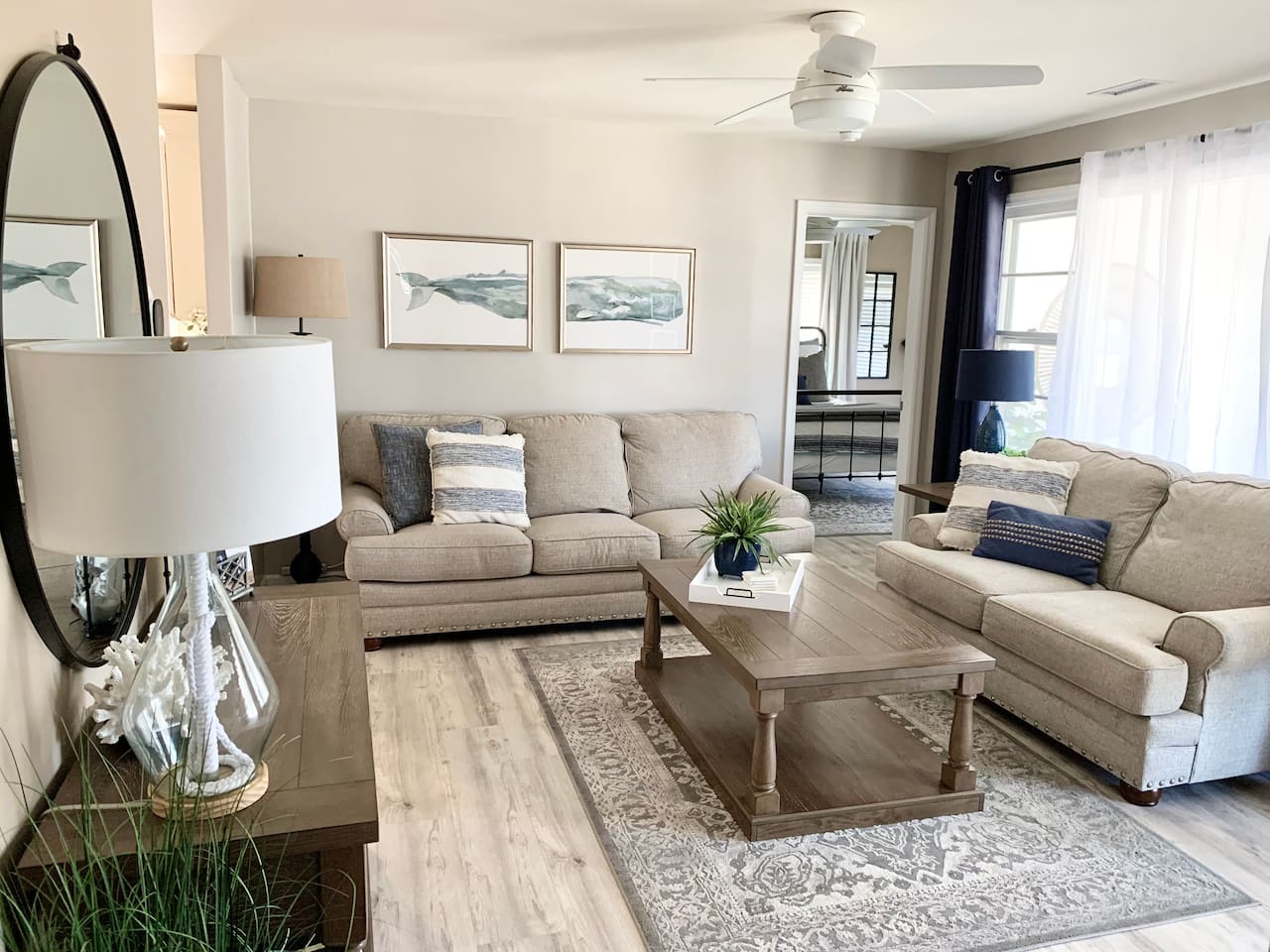 Relax in our coastal living room featuring comfy beige sofas, nautical pillows, and whale art. This bright, airy space with a rustic coffee table and patterned rug is perfect for family time after the beach.
