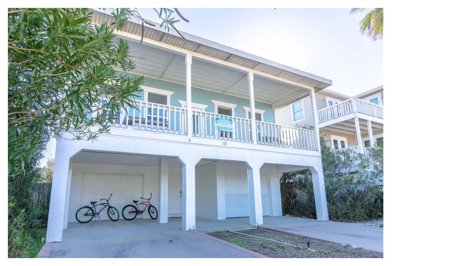 Charming coastal exterior with classic island architecture & covered parking below. The elevated design maximizes views and ocean breezes. Covered ground-level parking provides shade and protection for vehicles. The lush tropical landscaping adds privacy 