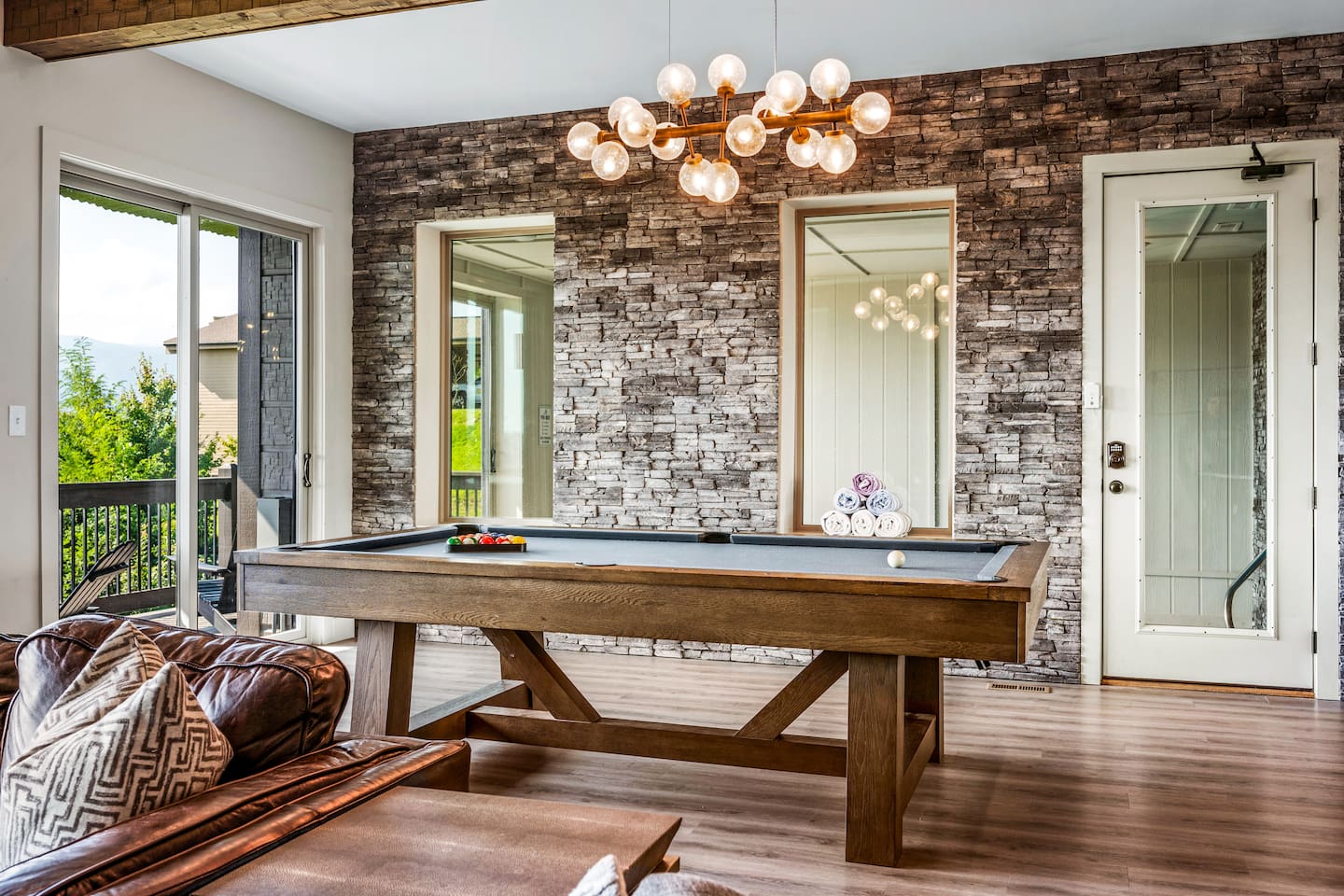 Modern Gatlinburg Airbnb cabin with game room featuring a full-size pool table, stone accent wall, designer chandelier, and mountain-view deck. Minutes to downtown Gatlinburg & Great Smoky Mountains National Park. Ideal getaway for families & groups.