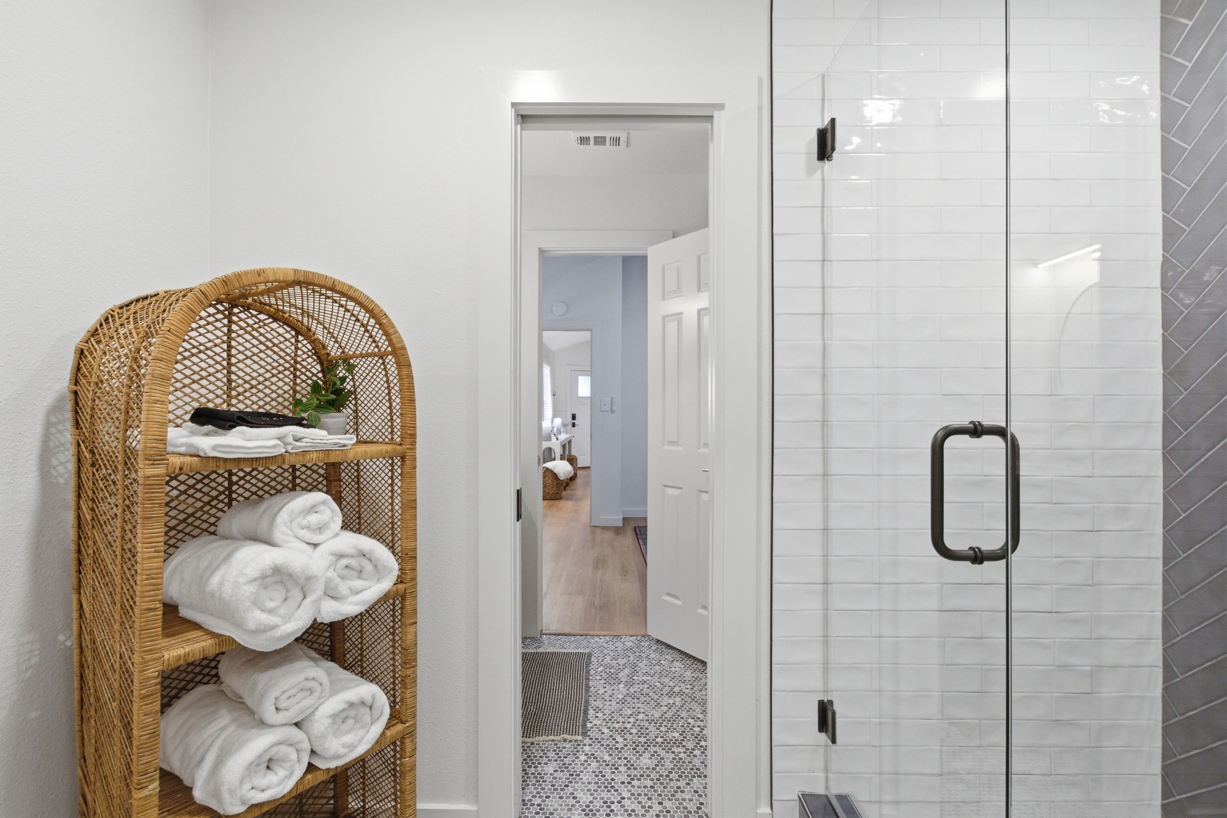 Fresh towels, woven storage tower, and standing shower with glass door. Each bathroom stocked with Ginger Lily Farms essentials for every guest.
