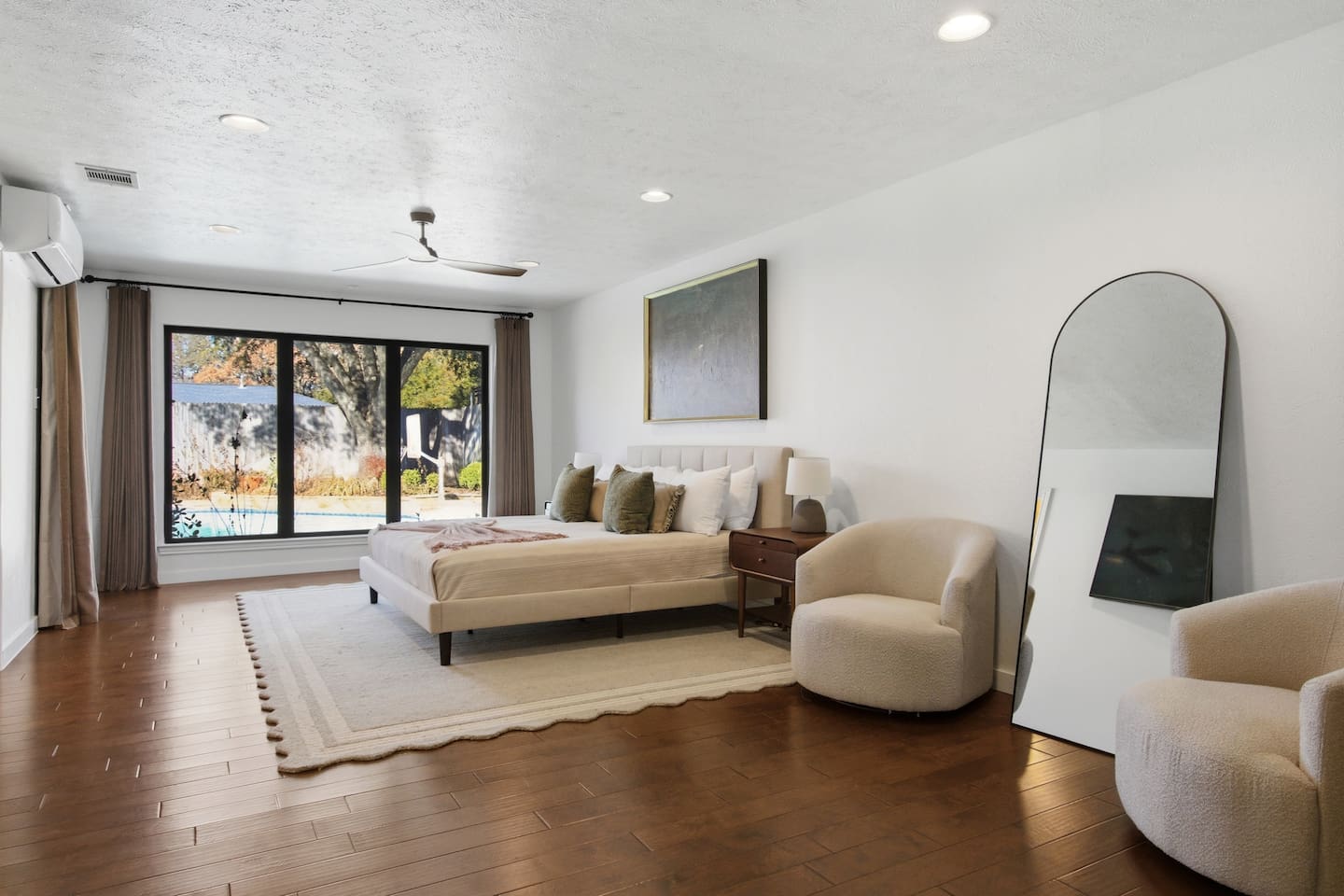 Spacious primary suite offering a king bed, 65” Smart TV, ceiling fan, sitting area, full-length mirror, room-darkening shades, and ample dresser storage, creating a relaxing and well-appointed retreat with easy backyard access.