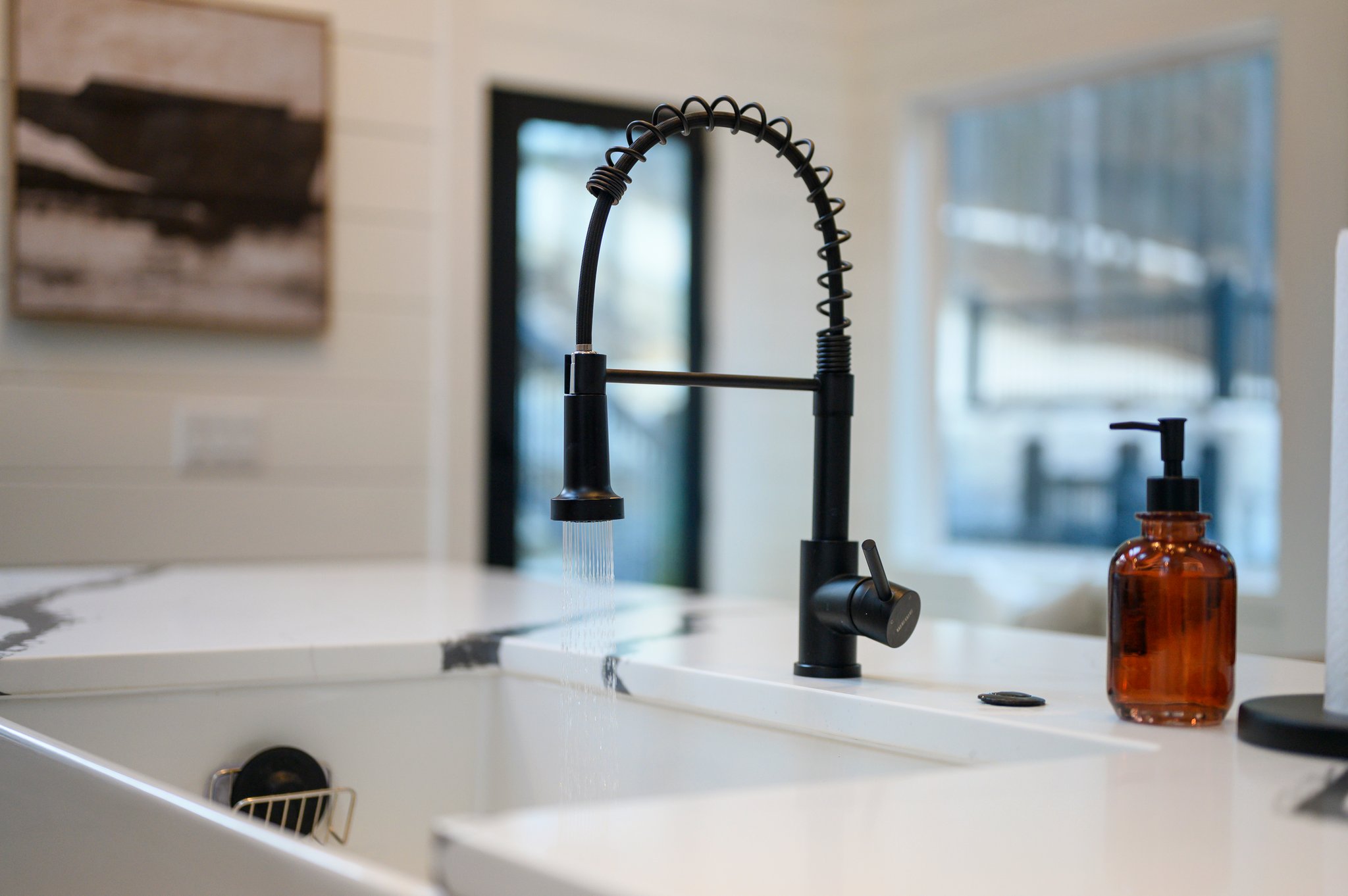 The oversized farmhouse sink with sleek black faucet makes cleanup easy while you enjoy peaceful forest views through the surrounding windows.