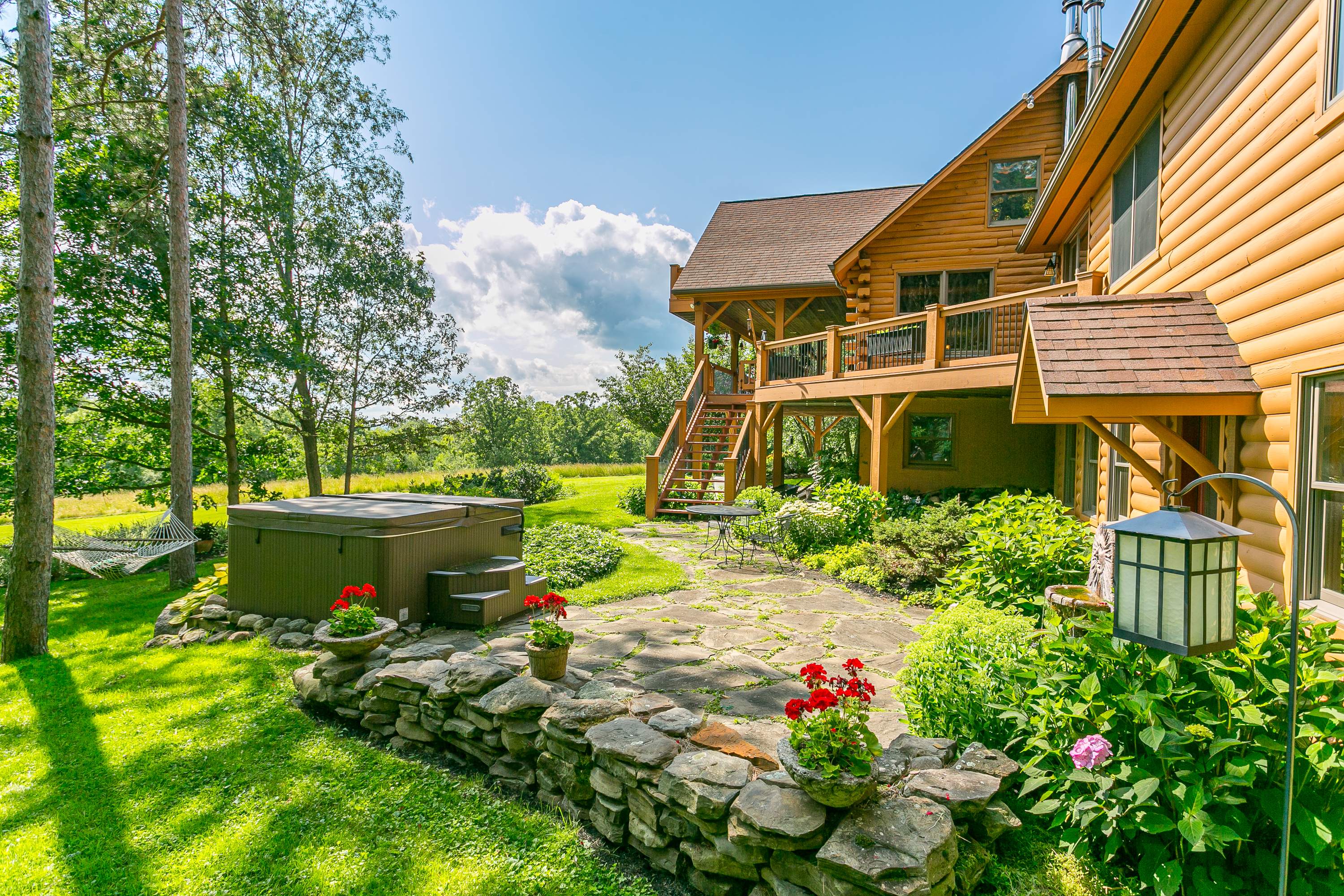 Enjoy a charming stone patio framed by vibrant flowers, greenery, and direct access to the hot tub from the downstairs king bedroom—your own garden sanctuary.