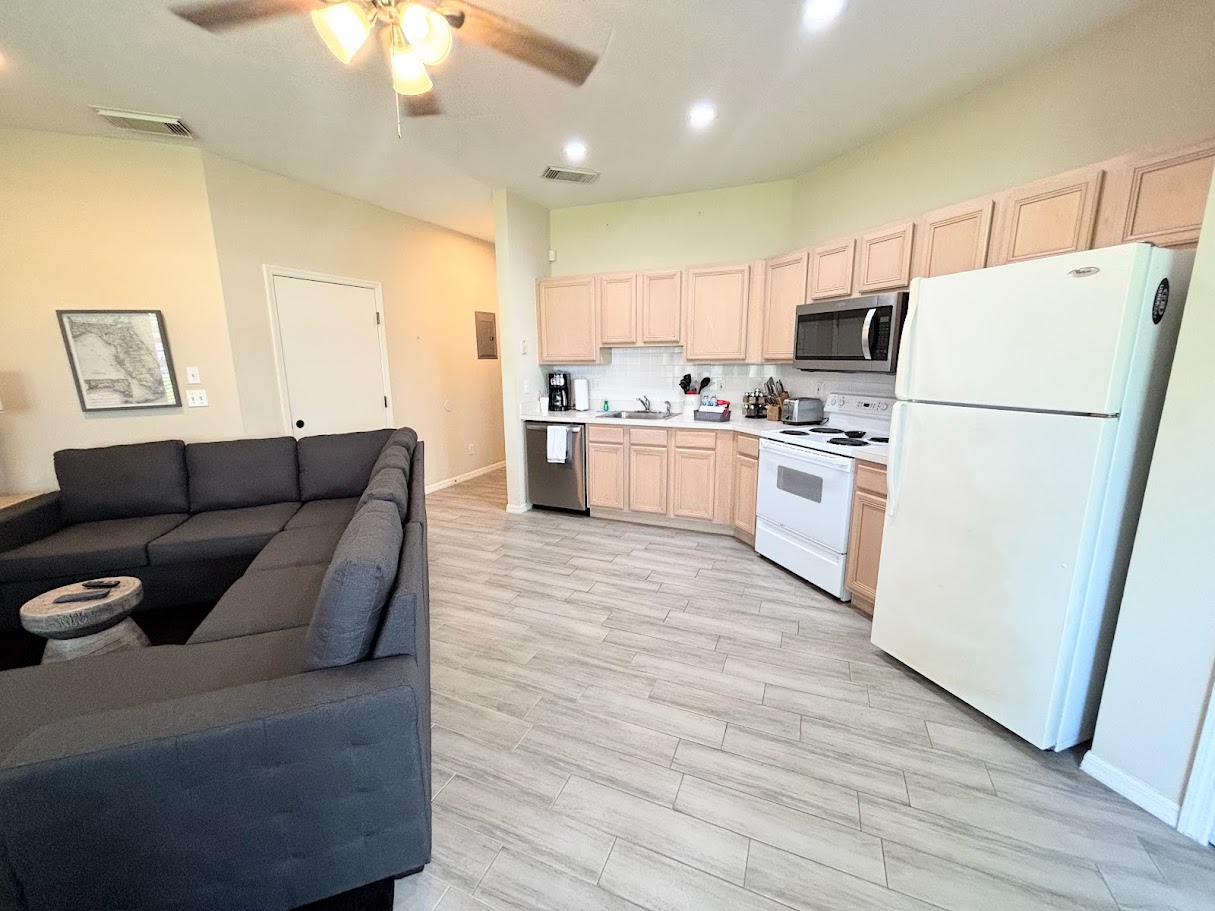 Open kitchen and living area with full-size appliances, wood-look flooring, and a comfortable sectional sofa.