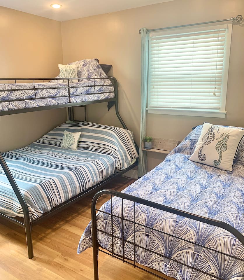 This cozy bunk room features a twin-over-full bunk bed and an additional twin bed, perfect for kids or extra guests. Coastal-themed bedding and seahorse pillows create a fun, nautical vibe for a relaxing stay.
