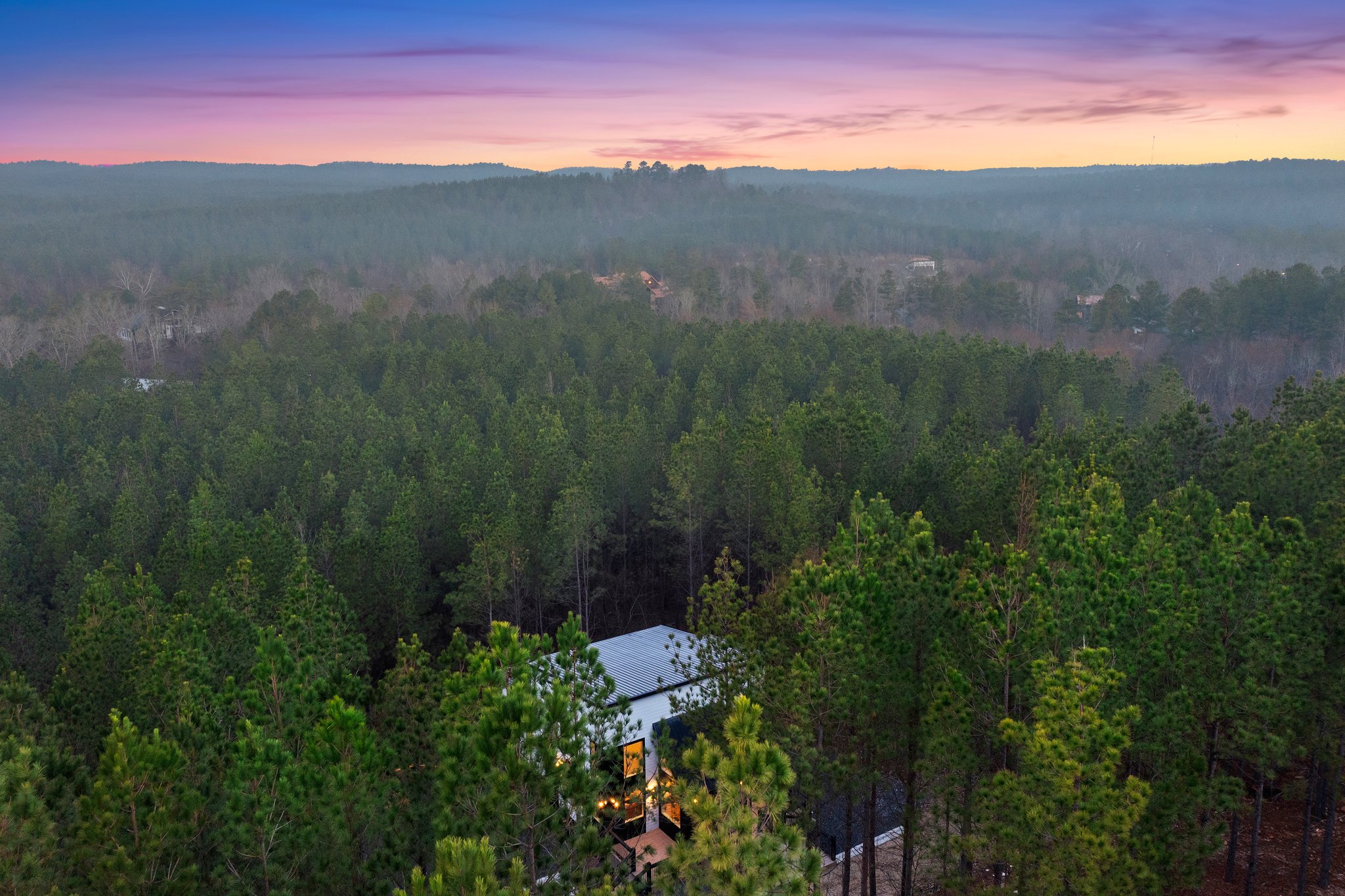 A modern cabin tucked into the treetops with sweeping forest views at sunset.