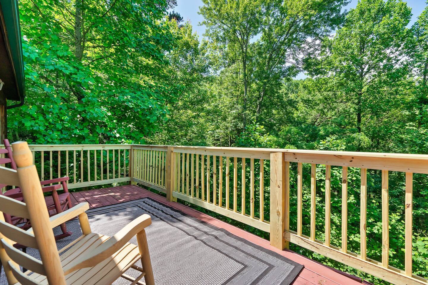 This spacious outdoor deck offers a tranquil retreat with comfortable rocking chairs and a wooden railing, providing panoramic views of the vibrant green treetops.