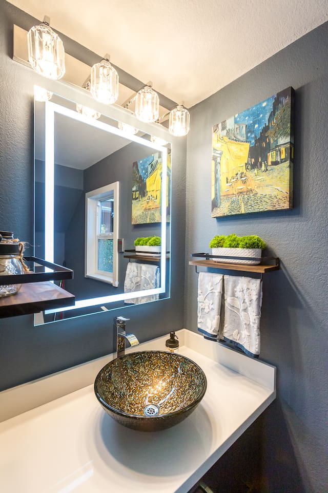 - Chic powder room with vessel sink and sleek illuminated vanity mirror  
- Dark accent wall and framed art create a sophisticated modern style  
- Floating shelves add both function and decorative touches to the space  
