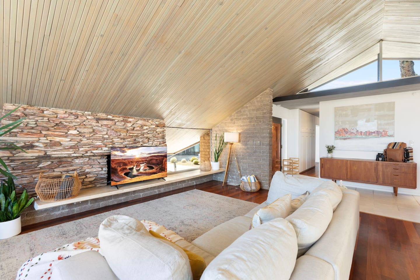 Mid-century charm meets modern comfort with a dramatic stone wall, soaring wood ceilings, and a bright, airy layout.