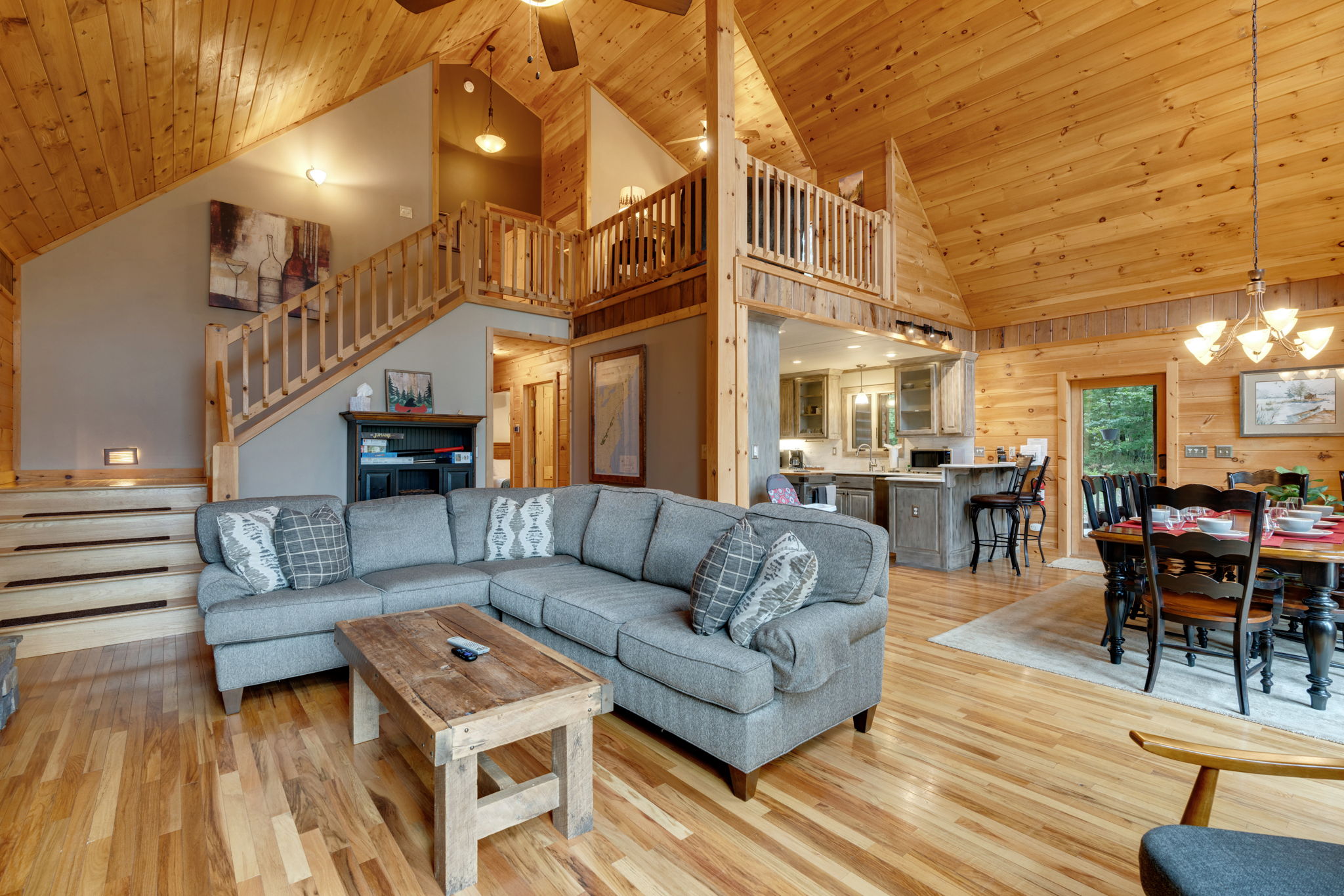 View of living room which also shows the kitchen, dining room, and the upstairs loft with sofa bed and library.