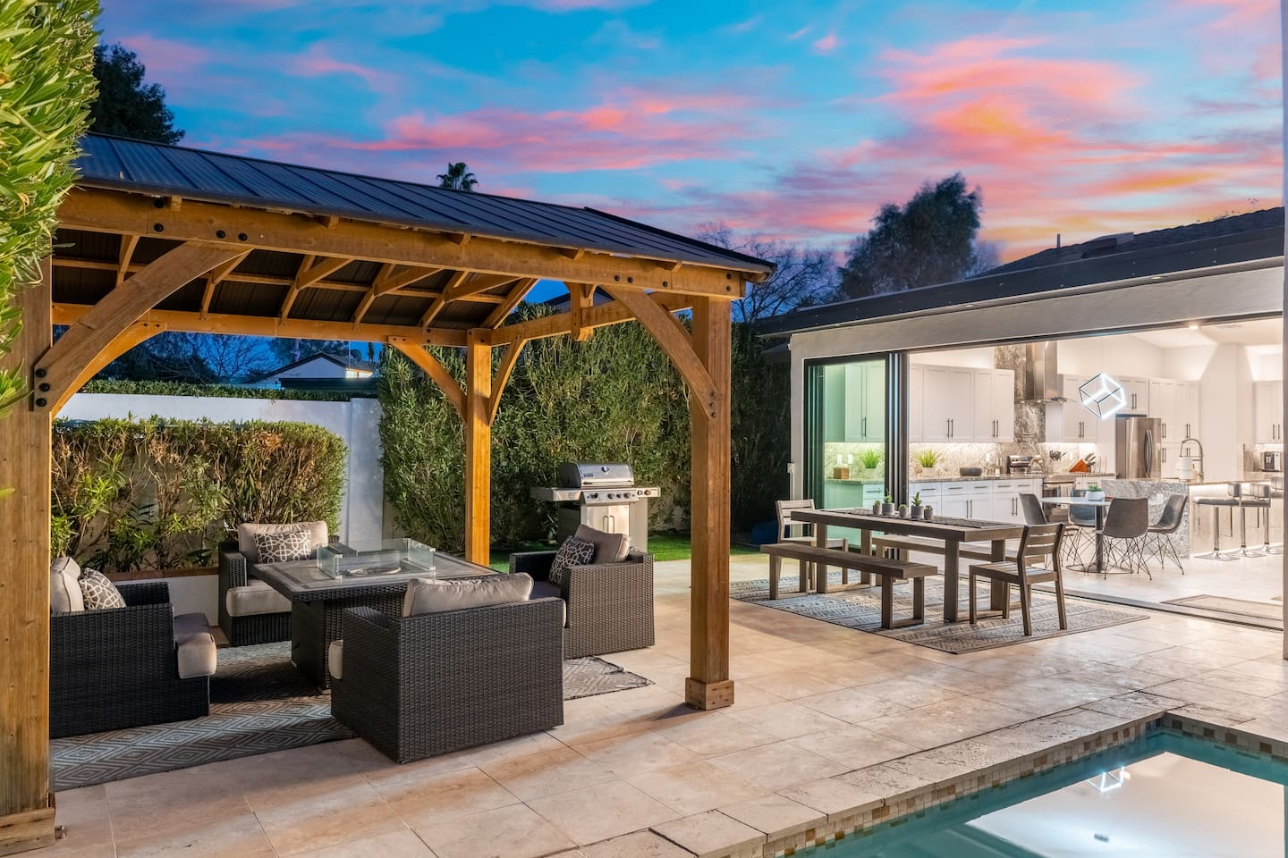 The wooden pergola offers an inviting setting with cushioned seating, a fire table, and a BBQ—ready for unforgettable nights.