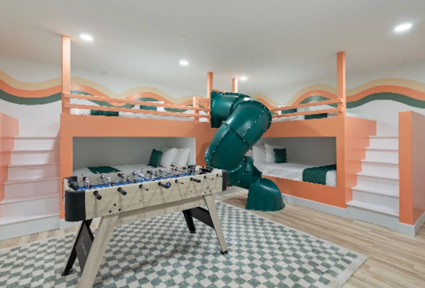 This isn't just a bedroom, it's a full-on kids' playground. Twin bunks tucked into a sunset-striped mural, a foosball table for rainy afternoons, and a slide connecting the top bunk straight down to the floor. 