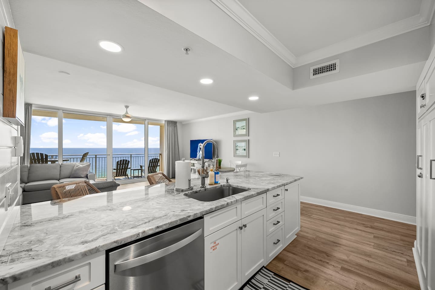 Modern kitchen with marble countertops and stainless steel appliances, opening to a bright living area and private balcony with breathtaking Gulf views.
