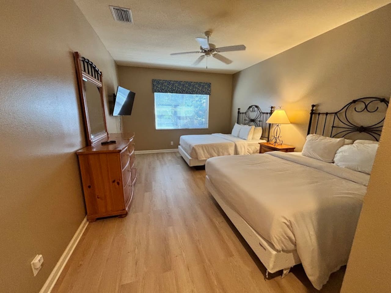 Spacious bedroom featuring two beds, ceiling fan, dresser storage, and a bright, relaxing layout.