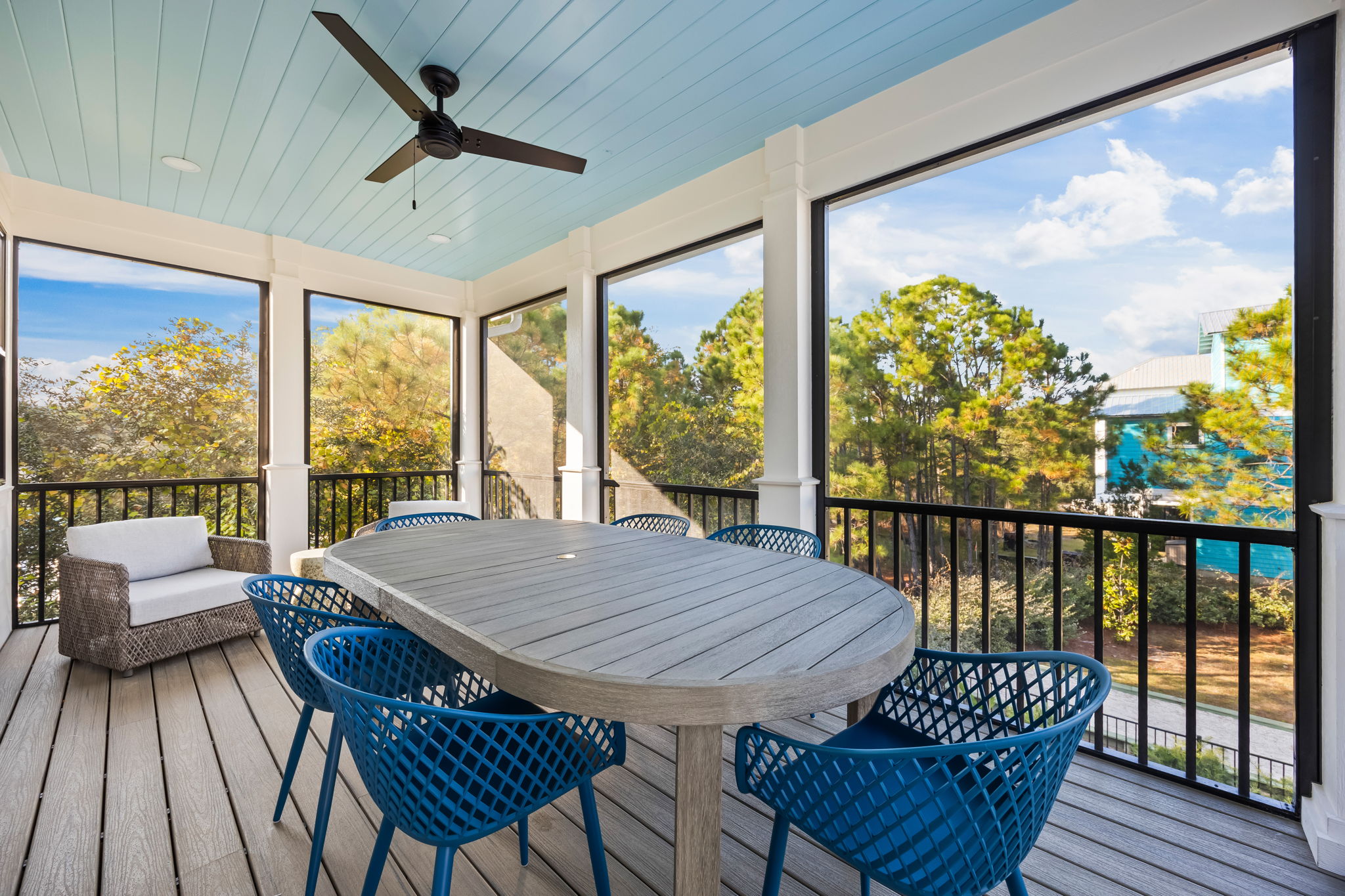 Screened upper porch dining just off the guest house kitchen, featuring a spacious table with coastal blue seating. This is the primary dining space for the home, overlooking the pool and perfect for shared meals, coffee, and relaxed evenings.